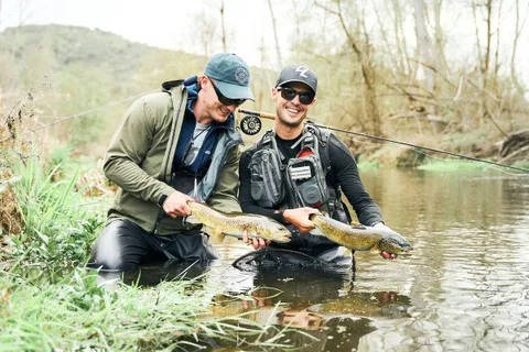 Two anglers landing a wild brown trout on a León river